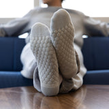 A person reclining on a blue couch with their feet up on a wooden table, wearing light gray textured socks with a raised bubble pattern on the soles. thumbnail