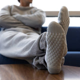 A person reclining indoors with their legs stretched out, wearing light gray knit socks with a raised bubble texture on the soles. The scene is shot from a low angle, with the person and a blue chair blurred in the background.