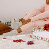 A woman sitting on a rug wearing fuzzy striped socks with Christmas decorations around her. thumbnail