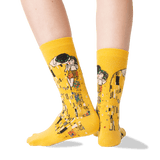 A pair of bright yellow crew socks with a Gustav Klimt 'The Kiss' graphic print, shown on a model's feet against a clean white background. thumbnail