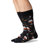A pair of black crew socks with a pattern of whiskey glasses, cigars, and cigars being lit by matches, shown on a person's legs against a white background.