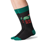 A pair of crew socks worn on a person's legs, featuring a dark charcoal gray body with a green turtle wearing a Santa hat and the text 'SLOW HO HO' in red, plus green cuffs, heels, and toes.