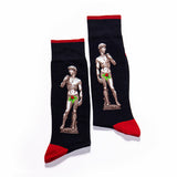 A pair of black crew socks with red cuffs, heels, and toes, featuring a graphic print of Michelangelo's David statue with a green bow-tie overlay.