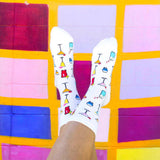 White crew socks with a colorful pattern of cocktail glasses, shown on a person's feet against a vibrant, multicolored tiled wall. thumbnail
