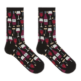 A pair of crew socks on a plain white background, featuring a black base with a repeating pattern of red wine bottles, wine glasses, corkscrews, and red raspberries.
