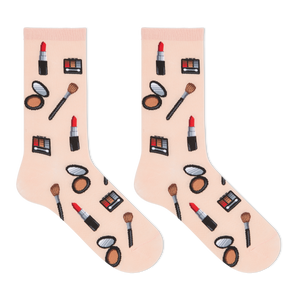 A pair of light pink crew socks with a repeating pattern of various makeup items, including lipstick, eyeshadow palettes, brushes, and compacts, displayed on a clean white background.