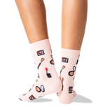 A pair of light pink crew socks with a makeup-themed print, worn on a person's feet against a clean white background. thumbnail