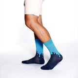 A person's legs wearing crew socks with a dark navy blue base and a bright blue dripping design along the top, shown against a plain white studio background. thumbnail
