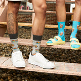 Two people standing on a metal walkway over gravel, wearing patterned crew socks. One person wears gray socks with a brown and orange sun glasses print, paired with white sneakers. thumbnail