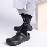 Person wearing black clogs and 'YES CHEF' socks on a white background