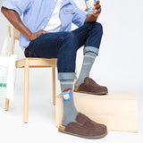 Person wearing gray socks with brand labels, sitting on a chair holding a can. thumbnail