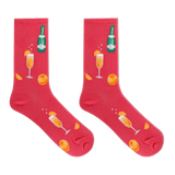 A pair of bright pink crew socks featuring a festive champagne-themed print with orange slices, champagne glasses, and a green champagne bottle, displayed against a solid white background.