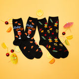 Two pairs of black socks with colorful designs on a yellow background with lemon slices and cocktail umbrellas. thumbnail
