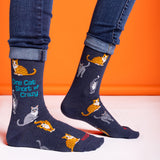 Navy socks with cat illustrations and text worn by a person against an orange background