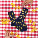 Navy blue socks with yellow pasta patterns on a red and white checkered tablecloth with scattered yellow pasta. thumbnail