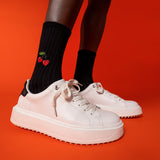White sneakers worn with black socks featuring red cherries on a red background thumbnail