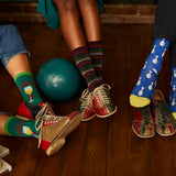 Three people wearing colorful socks and shoes with a bowling ball on a wooden floor.