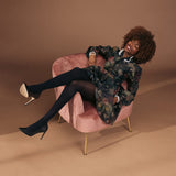 Woman sitting on a pink chair wearing a floral dress with black tights and heels on a brown background thumbnail
