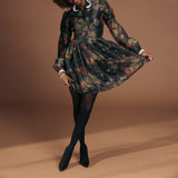 Woman wearing a floral dress with black tights and heels on a brown background