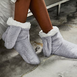 Gray fuzzy bunny slippers with white trim worn by a person on a concrete floor.