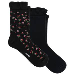 Two pairs of black crew socks with ruffled cuffs, one featuring a small pink and red floral pattern with green leaves, and the other solid black. The brand name 'it bell' is printed on the toe of the patterned sock.
