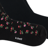 Black crew socks with a small pink and red floral pattern and green leaves, featuring the white text 'k.bell' near the toe, shown on a white background.
