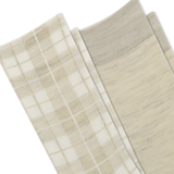 Close-up of folded socks in a soft neutral palette, showing a plaid pattern in cream and beige on one sock and a solid heathered light beige on the other, with a ribbed cuff. thumbnail