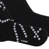 A close-up of a pair of black crew socks with a pattern of small pearl chains, featuring the white text 'k.bell' on the toe area, set against a plain white background.