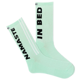 A pair of mint green sports crew socks with the text 'NAMASTE IN BED' printed on the side, featuring a reflective logo and a striped design with a visible logo on the calf area.
