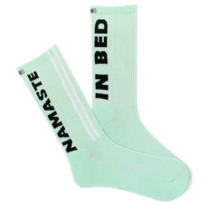 A pair of mint green sports crew socks with the text 'NAMASTE IN BED' printed on the side, featuring a reflective logo and a striped design with a visible logo on the calf area.