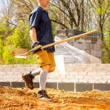 Man working with a shovel at a construction site with trees in the background