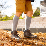 Person wearing yellow shorts, gray socks, and brown boots standing on a construction site.