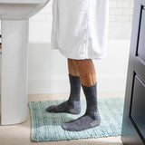 Person wearing gray socks on a light blue bath mat in a bathroom.