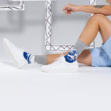 Person wearing white sneakers and patterned socks with Hokusai's 'The Wave' on a light gray background