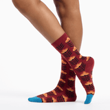 Red socks with a floral leaf pattern worn by a person on a white background thumbnail