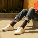 Person wearing white sneakers and patterned socks sitting on a concrete surface. thumbnail