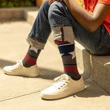 Person wearing white sneakers and colorful striped socks sitting on a concrete surface. thumbnail