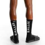 Black socks with 'BALLER' branding worn by a person on a white background thumbnail