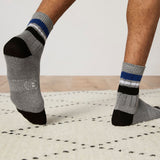 Gray socks with black toes and blue stripes worn by a person on a light wooden floor. thumbnail