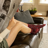 Woman sitting on a brown leather couch reading a newspaper, wearing red socks with black leopard patterns. thumbnail