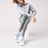 Person wearing a light gray tracksuit with blue jersey slippers on a white background
