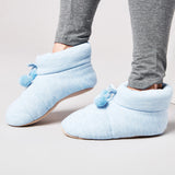 Light blue slip-on shoes with pom-poms worn by a person in gray pants on a light background