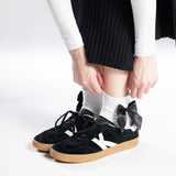 Black sneakers with white socks and a bow embellishment on a white background