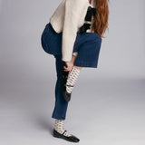 Person wearing blue jeans, a beige sweater, and patterned bow socks on a plain background