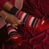 Red high-heeled shoes with a bow and red sheer striped socks on a red fabric background