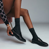 Person wearing black dress shoes and pointelle socks on a neutral background