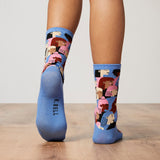 Blue socks with colorful patterns worn by a person on a wooden floor. thumbnail