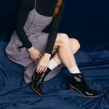 Person wearing a checkered dress and black boots with white socks sitting on a blue velvet background