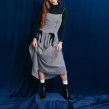 Person wearing a gray checkered dress with black accents against a blue backdrop
