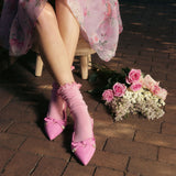 Person wearing pink high heels and pink slouch lettuce-edge socks with bow details on a brick floor, accompanied by a bouquet. thumbnail